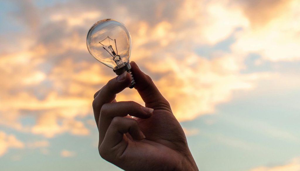 color photo of a person holding a lightbulb in front of a sunrise