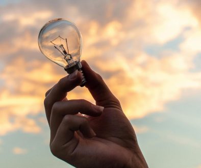 color photo of a person holding a lightbulb in front of a sunrise